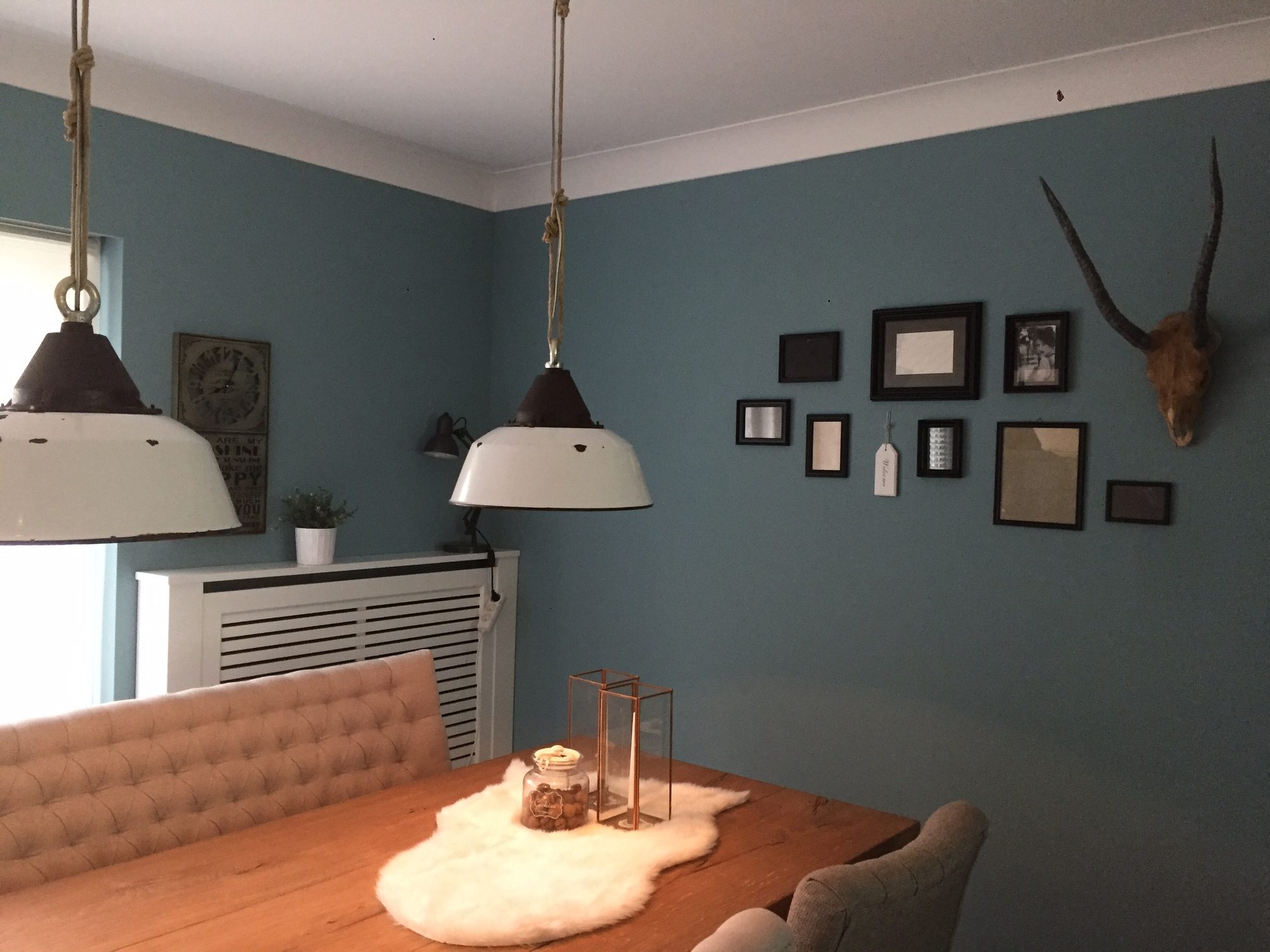 Eetkamer met blauwgroene wanden, fotolijsten en een gewei