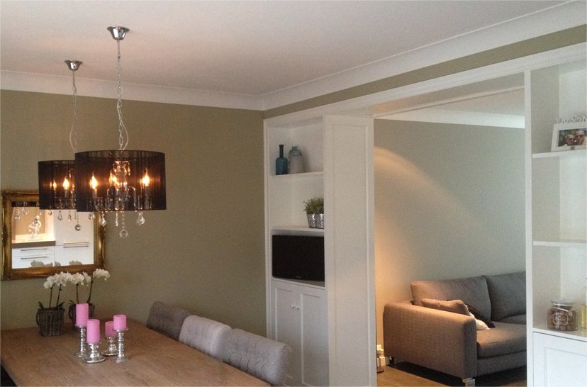Eetkamer met kroonluchter en witte inbouwkasten, wanden in warm taupe