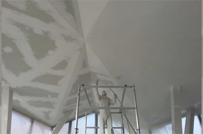 Spuiter in witte overall op een steiger spuit een plafond