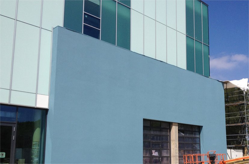 Bedrijfspand met een blauw gespoten gevel onder een glazen vliesgevel