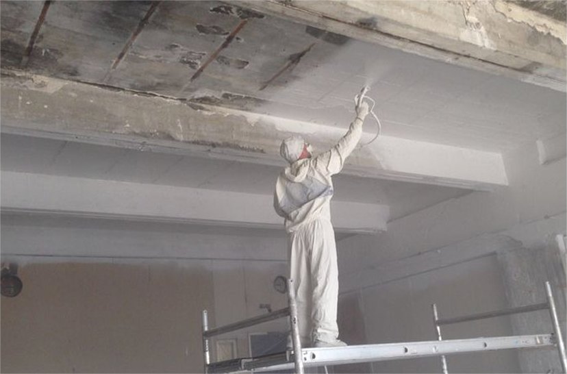 Spuiter in witte overall spuit een betonnen plafond vanaf een steiger